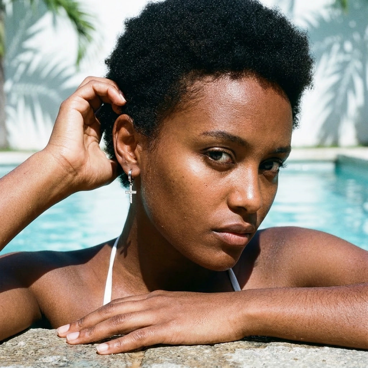 Pave Cross Huggie Hoops in Silver, worn by a tropical pool | SKU: 41006-silver