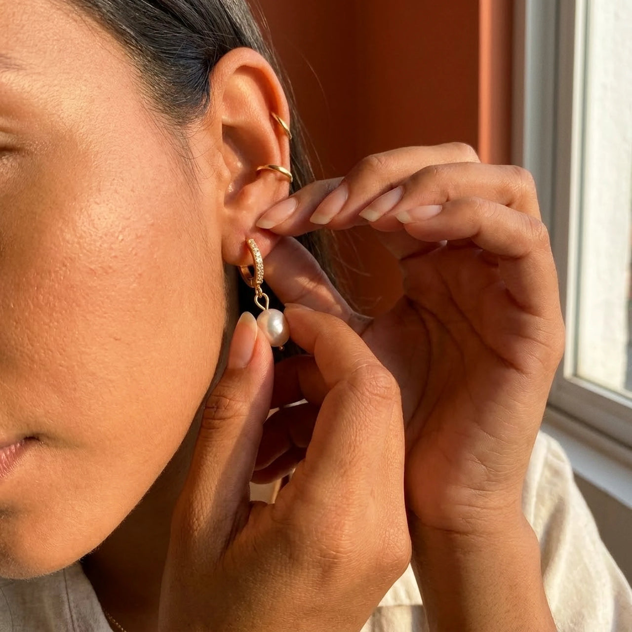Pearl Drop Huggie Hoops in Gold, being put on | SKU: 41003-gold
