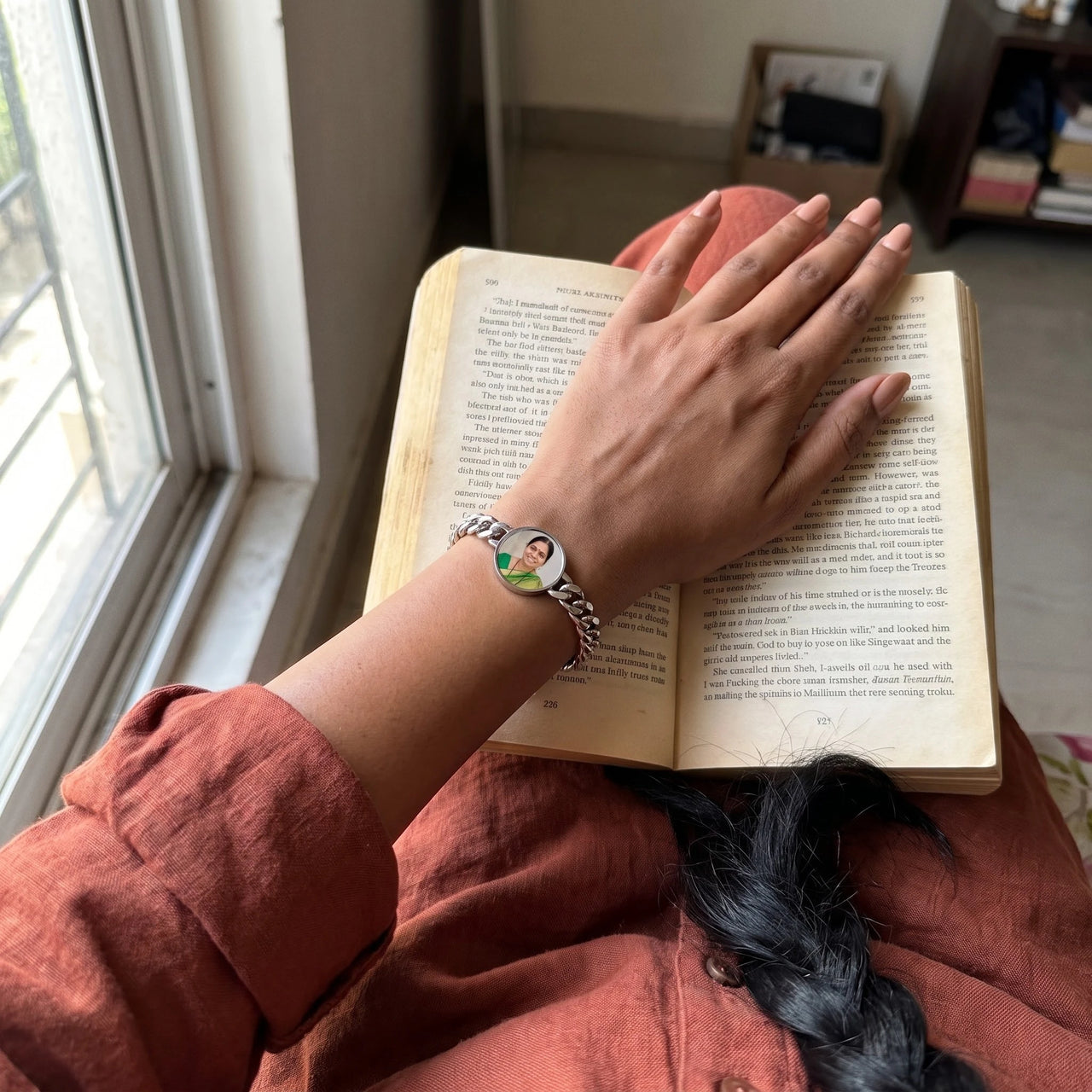 Her hand resting on an open book, the silver round photo bracelet with her grandmother's photo | SKU: TPH-RNDB-SILVER