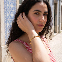 Thumbnail for Woman gently touching her Travel To Feel Alive bracelet in gold | SKU: ttfa-g